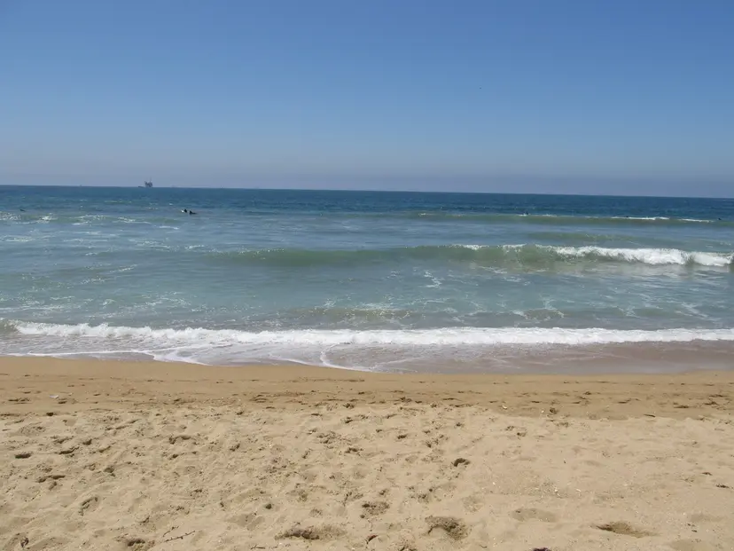 Small waves on the sand at Bolsa Chica State Beach, with an offshore oil platform on the horizon