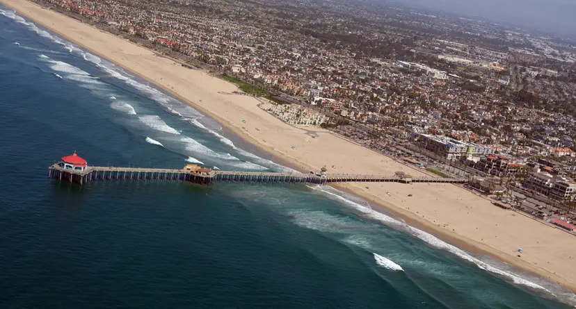Aerial view of the Huntington Beach Pier and the beach on both sides of it, with lines of surf breaking along the shore and the city behind