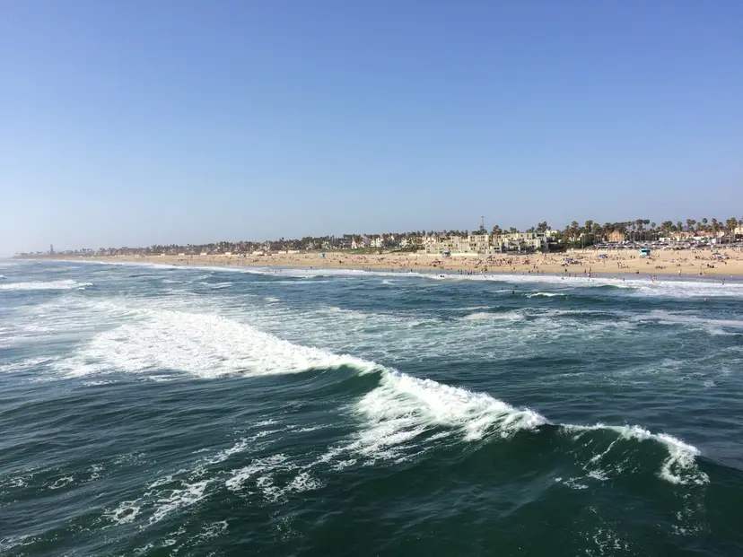 Waves breaking beside the Huntington Beach Pier, seen from the pier deck, with the beach and city behind