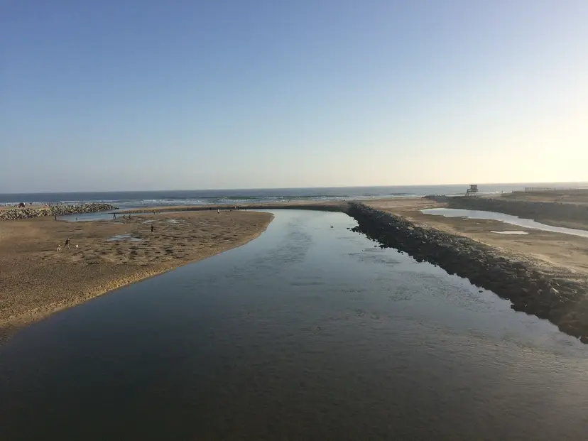 The Santa Ana River channel at sunset, running between its rock jetty and the sand toward the ocean