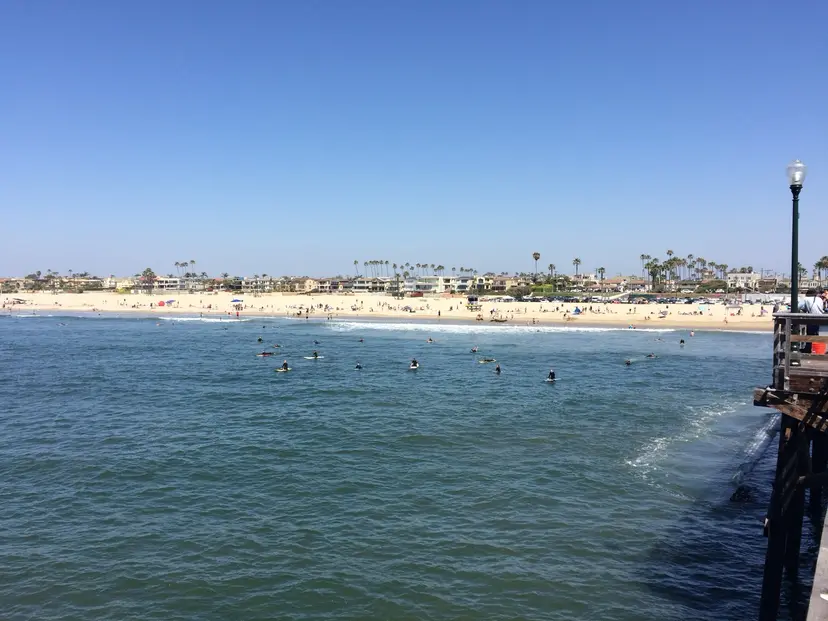 Surfers waiting in the water beside the Seal Beach Pier, seen from the pier